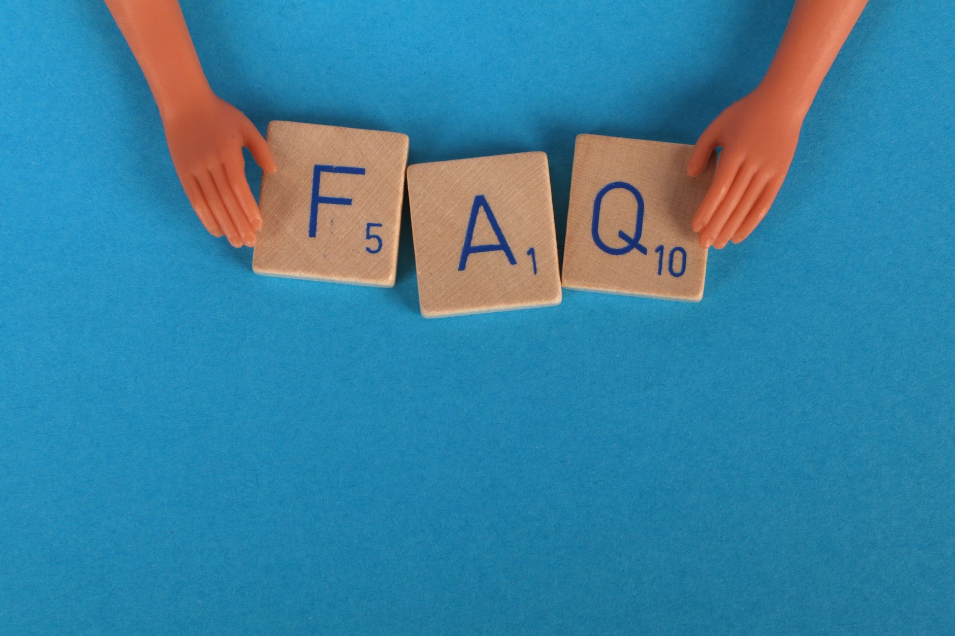 Flat lay of scrabble tiles spelling 'FAQ' with toy hands on a blue background, creating a conceptual image.