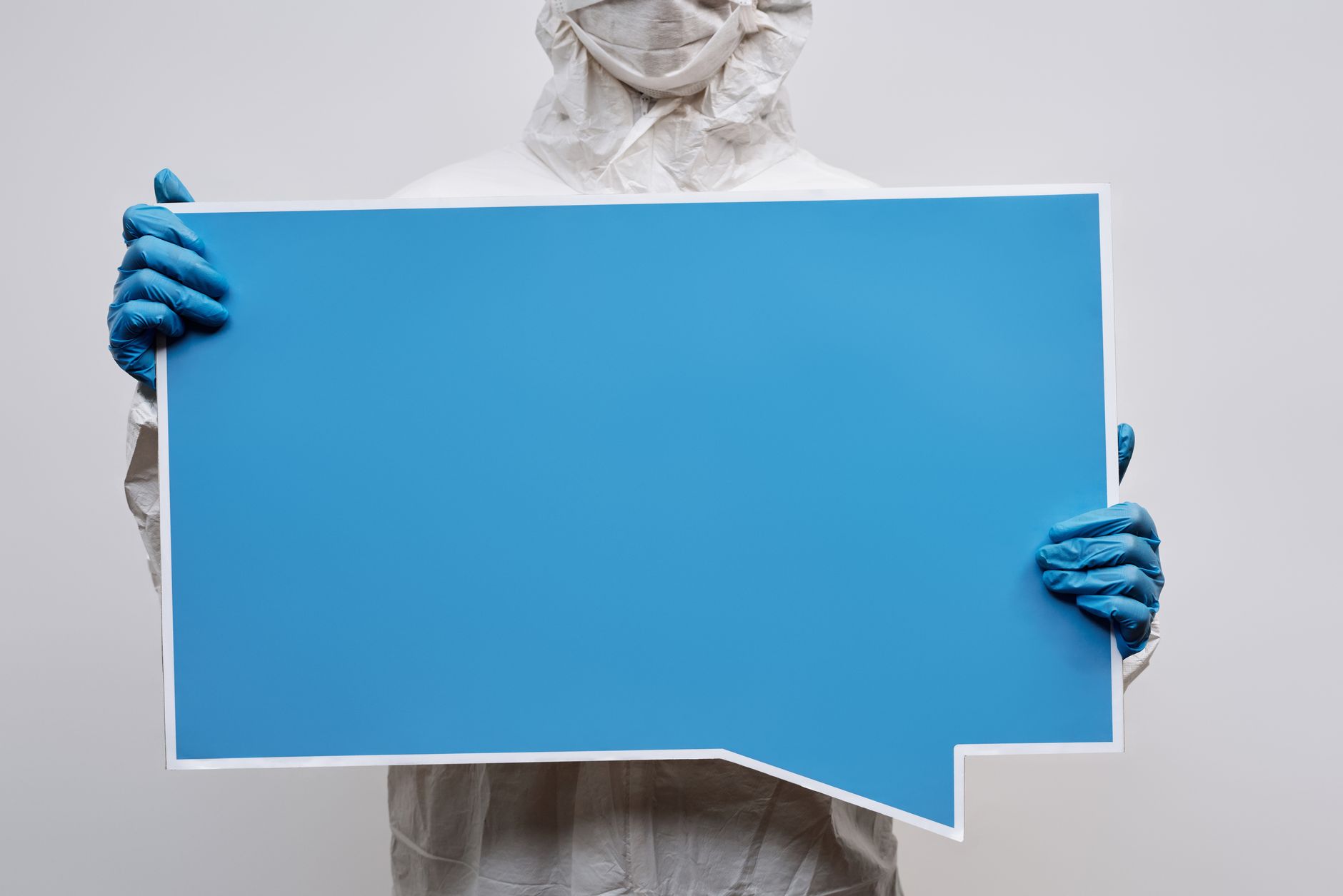 A person wearing protective gear holding a large blue speech bubble placard with copy space.