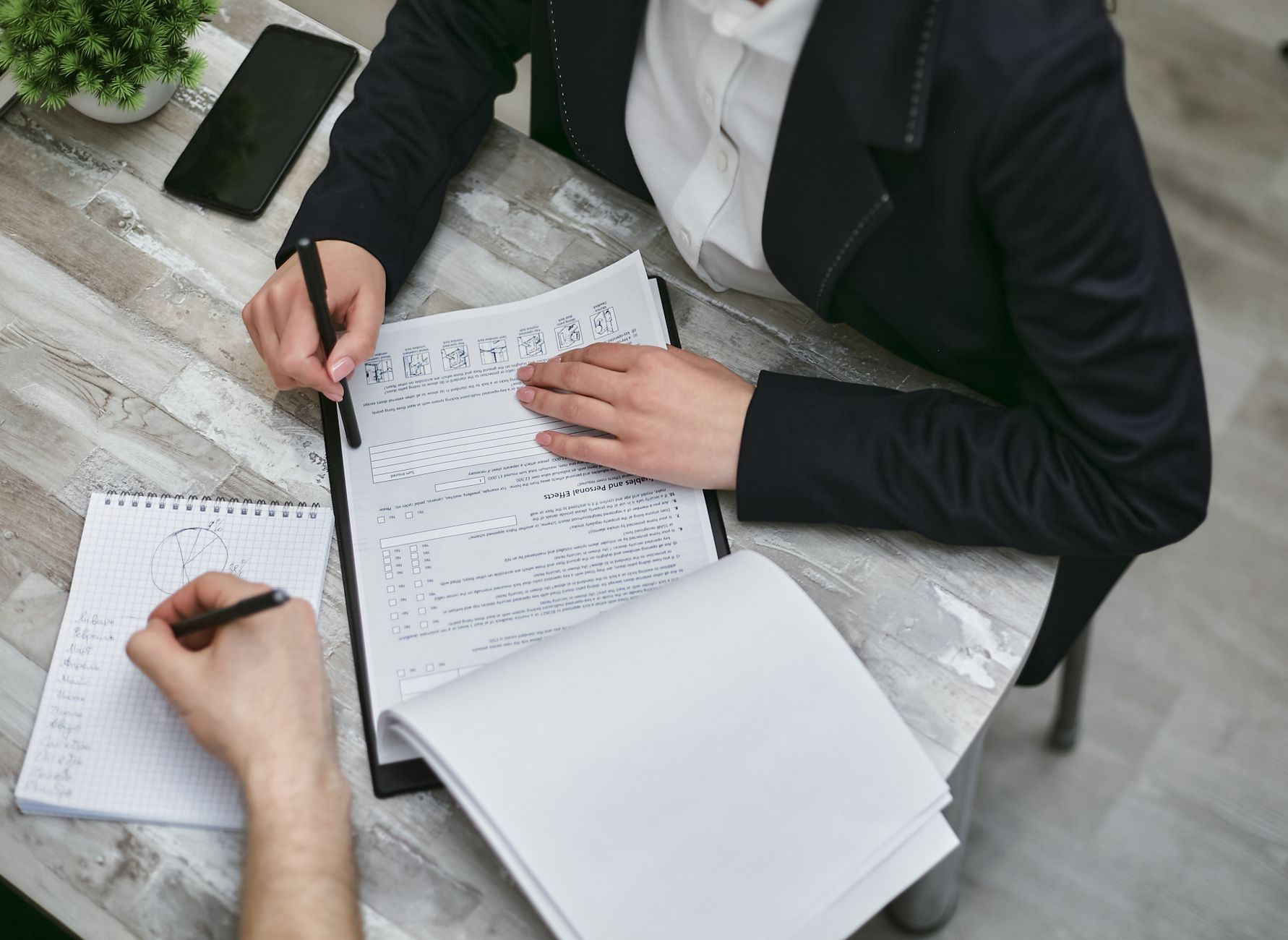 Two colleagues reviewing documents and taking notes during a business meeting.
