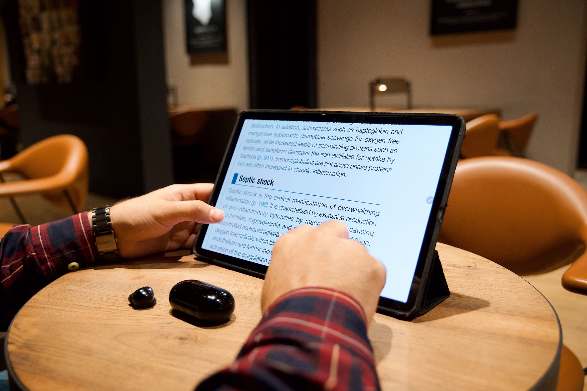 A close-up of a man reading a scientific article on his tablet while in a cozy cafe setting.